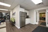 Modern apartment hallway with sleek wood flooring, stainless steel kitchen appliances, and a cozy seating area adorned with green cushions.