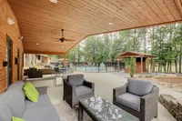 Inviting outdoor patio with cozy seating, wood-paneled ceiling, and views of a sparkling pool surrounded by lush trees.
