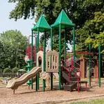 Charming playground with colorful slides and climbing structures, surrounded by lush greenery, ideal for family-friendly living.