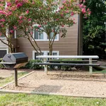 Charming apartment exterior view with a blooming garden, picnic bench, and barbecue grill area, perfect for outdoor gatherings.