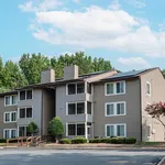Charming apartment complex with modern design, ample windows, and surrounded by lush greenery under a clear blue sky.