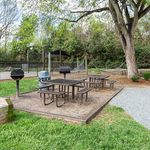 Inviting outdoor space with picnic tables and grills surrounded by lush greenery, perfect for social gatherings and relaxation.