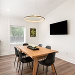 Elegant dining room featuring a modern wooden table, sleek black chairs, and a striking circular light fixture, enhanced by natural light from a large window.