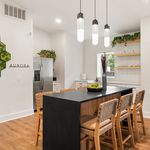 Sleek and modern kitchen with a stylish black island, wooden chairs, and elegant hanging lights, creating a perfect space for entertaining.