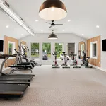 Modern fitness center with state-of-the-art treadmills, exercise bikes, and large windows offering lush garden views.