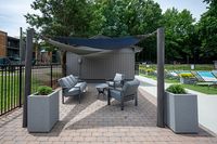 Modern outdoor seating area with sleek chairs, stylish canopy, and lush poolside loungers, creating a relaxing oasis.