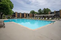 Inviting apartment complex with a large, refreshing swimming pool surrounded by sun loungers and lush greenery, perfect for relaxation and leisure.