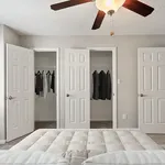 Elegant bedroom with plush bedding, featuring three white doors opening to spacious closets, highlighted by a stylish ceiling fan.