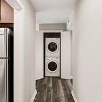 Modern apartment hallway featuring sleek laminate flooring and an in-unit stacked washer and dryer discreetly tucked behind folding doors.