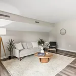 Chic modern living room with stylish decor, featuring a cozy gray sofa, sleek black chair, wooden coffee table, and elegant floor lamp, complemented by a neutral area rug and lush green plants.