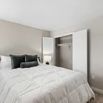 Inviting bedroom with a plush white comforter, elegant gray pillows, and a spacious open closet, perfect for modern living.