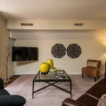 Elegant living room with modern decor, featuring a stylish glass coffee table, vibrant accents, and mounted TV.