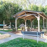 Charming outdoor pavilion with cozy seating and hammocks, surrounded by lush greenery, offering a relaxing community space.