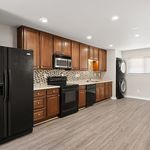 Contemporary kitchen with sleek black appliances, elegant wooden cabinetry, and stylish backsplash, featuring a convenient in-unit washer and dryer.