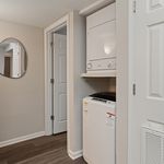 Modern laundry area with stacked washer and dryer, sleek flooring, and stylish mirror in a cozy apartment setting.