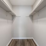 Spacious walk-in closet with sleek shelving and elegant wood-style flooring, offering ample storage room and modern style.