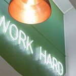 Chic interior space featuring a neon 'Work Hard' sign on a vibrant green wall, illuminated by a modern ceiling light.