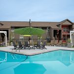 Inviting apartment complex with a sparkling outdoor pool, surrounded by stylish lounge chairs and vibrant green umbrellas.