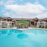 Inviting apartment complex with modern architecture, featuring a sparkling swimming pool, shaded lounge area, and beautifully landscaped surroundings.