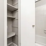 Bright and efficient bathroom setup featuring a built-in shelving unit and gleaming tiled bathtub, offering practicality and style.