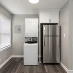 Modern laundry area with a sleek stackable washer-dryer combo next to a stainless steel refrigerator, accented by stylish cabinetry and elegant flooring.