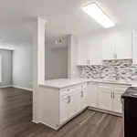 Modern kitchen with sleek white cabinetry and stylish backsplash, opening into a spacious living area with elegant wood flooring.
