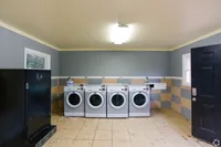 Inviting and spacious laundry room featuring four sleek, modern washing machines, complemented by a stylish striped wall design and practical tiled flooring.