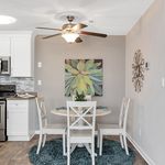 Charming dining area featuring a modern round table set with white chairs, elegant wall art, and a chic kitchen backdrop.