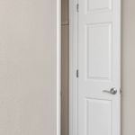 Sleek white interior door with modern handle, opening to reveal a cozy closet space, perfect for organized living.