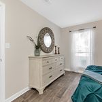 Elegant bedroom with a chic dresser, round decorative mirror, and sunlit window, showcasing modern charm and comfort.
