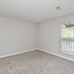 Bright and airy empty room with soft carpet flooring and a large window overlooking green scenery.