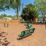 Inviting dog park with green agility equipment, open space, and shaded seating surrounded by lush trees.