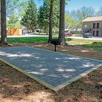 Charming outdoor communal space with brick patio and barbecue grill surrounded by lush greenery and mature trees.