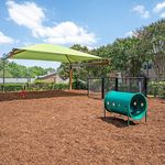 Charming outdoor dog park with a vibrant green shade, playful tunnel, and lush greenery, perfect for pet-friendly living.