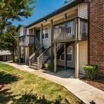 Charming two-story apartment building with private balconies, set amidst lush greenery and sunny pathways.