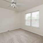 Bright, airy bedroom with large window and ceiling fan, featuring plush carpeting and a neutral color palette for a cozy ambiance.