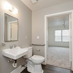 Bright, modern bathroom featuring sleek fixtures, a large mirror, and a view into a sunlit room with plush carpeting.