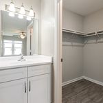 Bright bathroom with a sleek white vanity and a spacious walk-in closet, featuring elegant lighting and modern finishes.