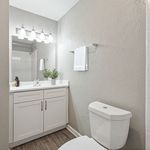 Elegant bathroom featuring a sleek vanity with bright lighting, contemporary fixtures, and a modern white toilet set against a soothing gray wall.