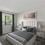 Elegant bedroom with chic decor, featuring a plush bed with gray bedding, stylish nightstands, and modern lamps, complemented by a scenic artwork and abundant natural light from a large window.
