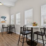 Bright and airy residential dining area with modern high-top tables, stylish artwork, and natural light streaming through large windows.