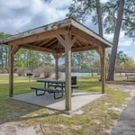 Inviting outdoor pavilion with a picnic table and grill, surrounded by lush trees and adjacent to tennis courts.
