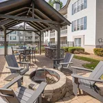 Charming outdoor patio area with cozy fire pit, shaded seating, and modern grill, perfect for entertaining at a stylish apartment complex.