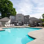 Inviting outdoor swimming pool with lounge chairs at a modern apartment complex, set against a lush green backdrop and clear blue skies.