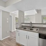 Bright and modern kitchen with sleek countertops, dual sink, and open view to a sunlit living area.