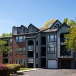 Charming apartment exterior with modern architecture, brick and siding facade, and lush green surroundings under a clear blue sky.