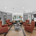 Inviting common area with stylish orange armchairs, sleek grey cabinets, and a view of the lush outdoor patio.