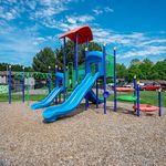 Bright and colorful playground with blue slides and climbing structures, set in a lush green community park.
