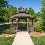 Charming wooden gazebo nestled in lush green garden setting beneath a clear blue sky, perfect for relaxation and outdoor gatherings.