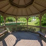 Charming wooden gazebo with inviting benches, nestled in a lush garden setting, perfect for relaxation and outdoor enjoyment.